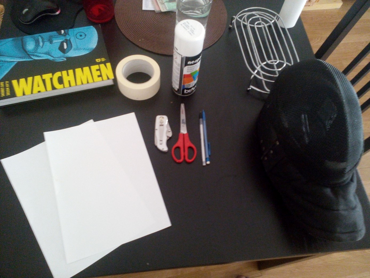 Le masque, le ruban, les feuilles, le crayon, les ciseaux et la peinture réunis sur la table de Michel.