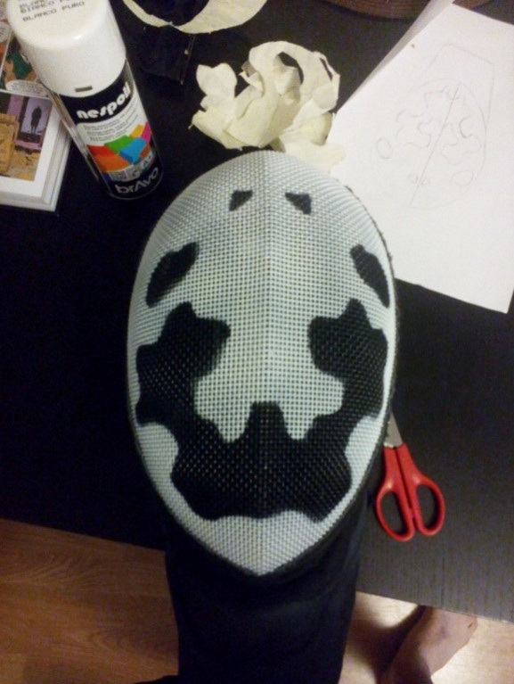 Masque terminé de Michel : motif noir irrégulier sur une grille peinte en blanc, au-dessus d’une bavette noire.